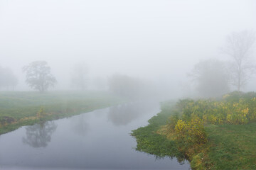Naklejka na ściany i meble Foggy morning on a river with an autumn landscape