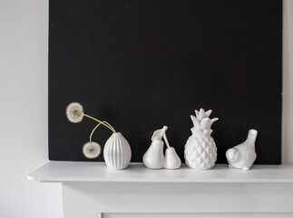 White figurines of pineapple, pear, bird, a vase with two dandelions on the background of a black...