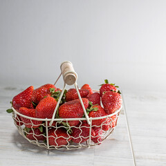 White metal basket with wooden handle with fresh strawberries on beige table