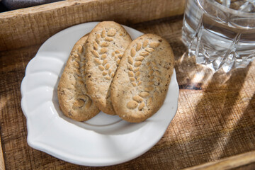 A white cup of coffee, a glass of water, a long cupronickel spoon with a twisted handle and a saucer with lemon for breakfast on a wooden tray, a rag napkin on a gray sofa.