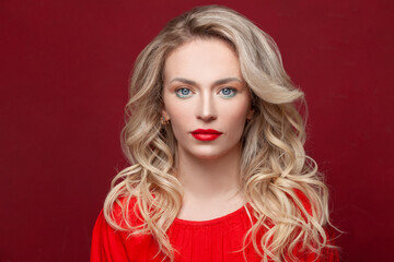 Perfect woman fashion model with healthy blonde curly hair styling and makeup on red background