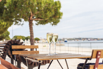 Two glasses of sparkling wine on a wooden table outside with a sea view