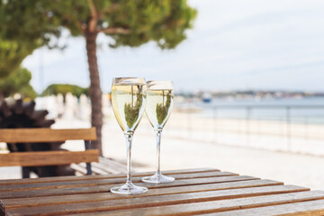 Two glasses of sparkling wine on a wooden table outside with a sea view