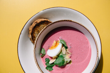 cold beet soup with kefir, fresh herbs, boiled egg and slice of grilled bread on the table of cafe summer terrace