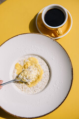 Oatmeal porridge with bowl of passion fruit ice cream and coconut flakes and cup of filter coffee. Yellow background of summer terrace
