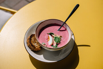 cold beet soup with kefir, fresh herbs, boiled egg and slice of grilled bread on the table of cafe summer terrace