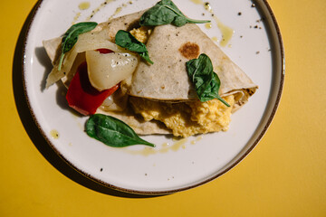 Omelette in lavash with slices of pepper and spinach leafs on a plate