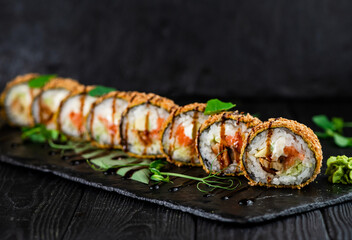 Japanese tempura hot sushi roll on Black slate stone plate on wooden background. sushi pieces with salmon, eel, cucumber, cream cheese, avocado wrapped in rice with crunchy seaweed on top with greens
 - Powered by Adobe