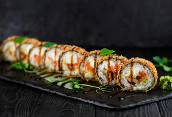 Fotobehang Japanese tempura hot sushi roll on Black slate stone plate on wooden background. sushi pieces with salmon, eel, cucumber, cream cheese, avocado wrapped in rice with crunchy seaweed on top with greens  © Art Food