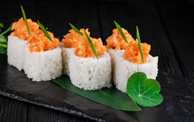 Close up to Japanese sushi roll on black slate stone plate on wooden background. sushi pieces with minced salmon fillet on top served with spring onion scallions and with greens
