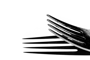Closeup of a fork horizontally on a white surface, with a harsh shadow