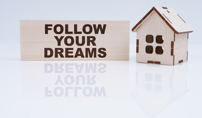 There is a wooden house and a sign on the table - Follow your Dreams