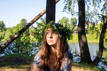 Beautiful blue eye girl in floral crown and dress in the sunnt sumer forest on river side