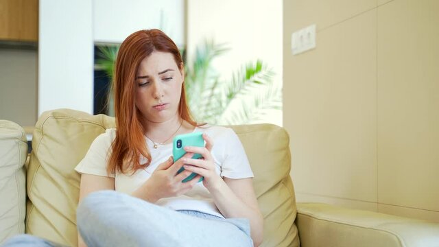 young woman or girl misses sitting on sofa with phone in hands. Lonely female student upset at home alone. Unhappy upset millennial female suffer from depression or solitude, feel lonely. Miscarriage