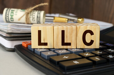 On the table are money, a calculator, a notebook and cubes with the inscription - LLC