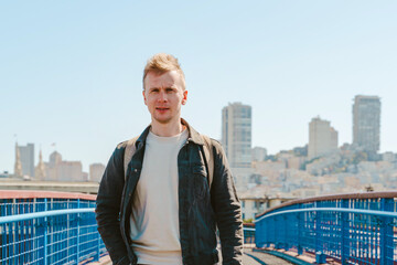 A young man walks down a street with a view of the city of San Francisco