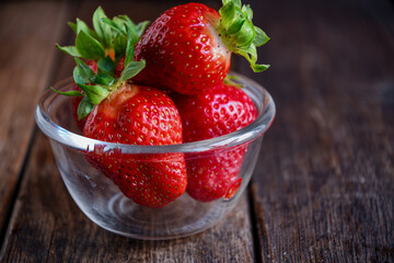 Strawberries in a glass dish on an old wooden table. Cooking in the kitchen.