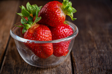 Strawberries in a glass dish on an old wooden table. Cooking in the kitchen.