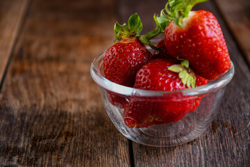 Strawberries in a glass dish on an old wooden table. Cooking in the kitchen.
