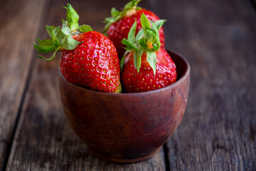 Strawberries in a wooden bowl on an old wooden table. Cooking in the kitchen.