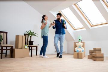 House moving concept - young caucasian couple dancing and drinking champagne to celebrate their very first day in new home.