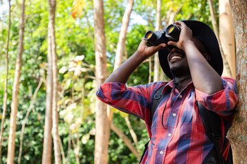 Happy Africa American hipster man backpack using binocular for search animal in nature public park...
