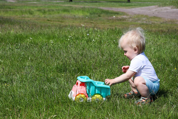 small one year old boy child playing with toy truck car in the park