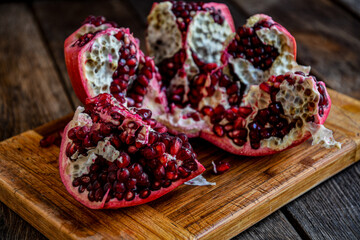 Sliced, peeled pomegranate fruit lies on a kitchen board on a wooden table.