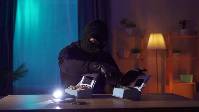 thief in a balaclava finds jewelry and money on a table in the house