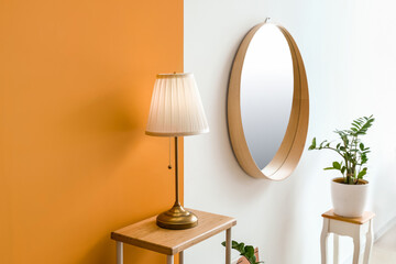 Modern lamp on table and mirror hanging on color wall in room