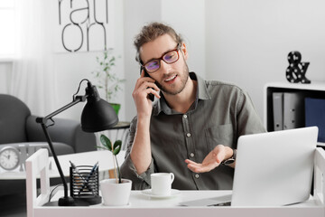 Handsome young man talking by mobile phone in office