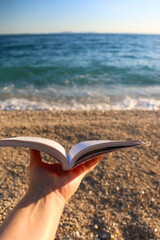 Hand holding open book on a beach. Selective focus.