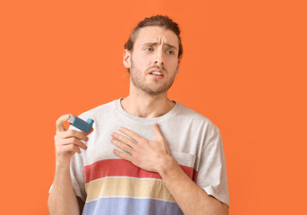 Young man with inhaler having asthma attack on color background - obrazy, fototapety, plakaty