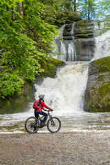 pretty woman with electric mountain bike admiring the Eibele Falls in the Allgaeu mountains near...