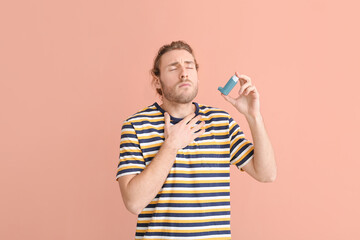 Young man with inhaler having asthma attack on color background