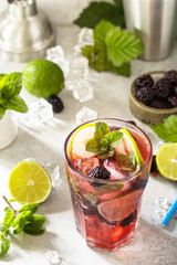 Summer blackberry mojito or blackberry soda. Refreshing summer drink with blackberry, mint, lime and ice on a stone table.