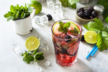 Summer blackberry mojito or blackberry soda. Refreshing summer drink with blackberry, mint, lime and ice on a stone table. 