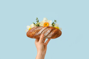 Woman holding tasty fresh bread with flowers on color background