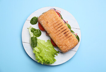 Board with tasty ciabatta sandwich on color background