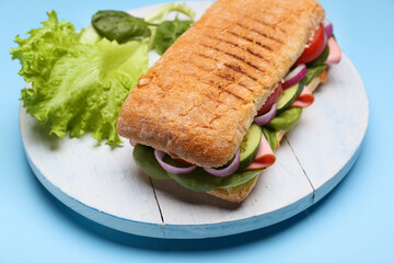 Board with tasty ciabatta sandwich on color background