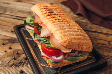 Board with tasty ciabatta sandwich on wooden background