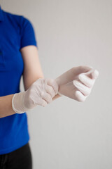 A young woman puts a white latex disposable medical glove on a hand on the white backgrounds.