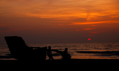 Naklejka na ściany i meble Silhouette of a Boat and two men on a southern Sri Lankan Beach when the sun is setting on to the Indian Ocean