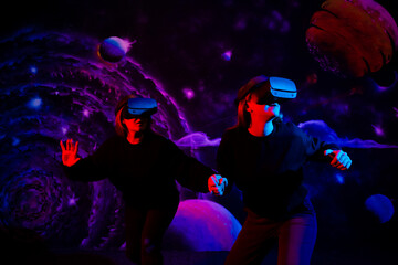 Two girls friends in virtual glasses are holding hands in the playroom in neon light