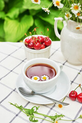 Breakfast outside. Cup of tea, strawberries, cherries, chamomile bunch on table. Summer picnic. Good morning concept
