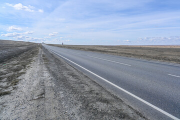 Highway road in the steppes, bushes, grass and cloudy sky. Spring.