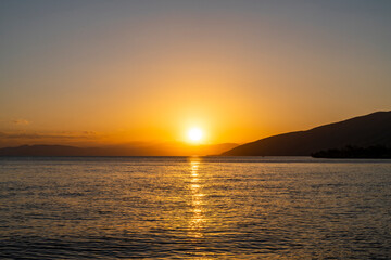 Beautiful golden sunset over the lake. The summer sun goes down behind the mountains.