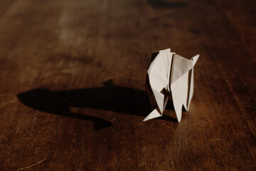 Origami elephant made of brown paper over wooden background.