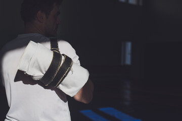 Martial arts lifestyle. A man in a ray of sunlight with a kimono wrapped in a black belt behind his...