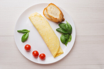 French three eggs omelette with spinach leaves, cherry tomatoes for a breakfast on a white plate on wooden background. Top view.
